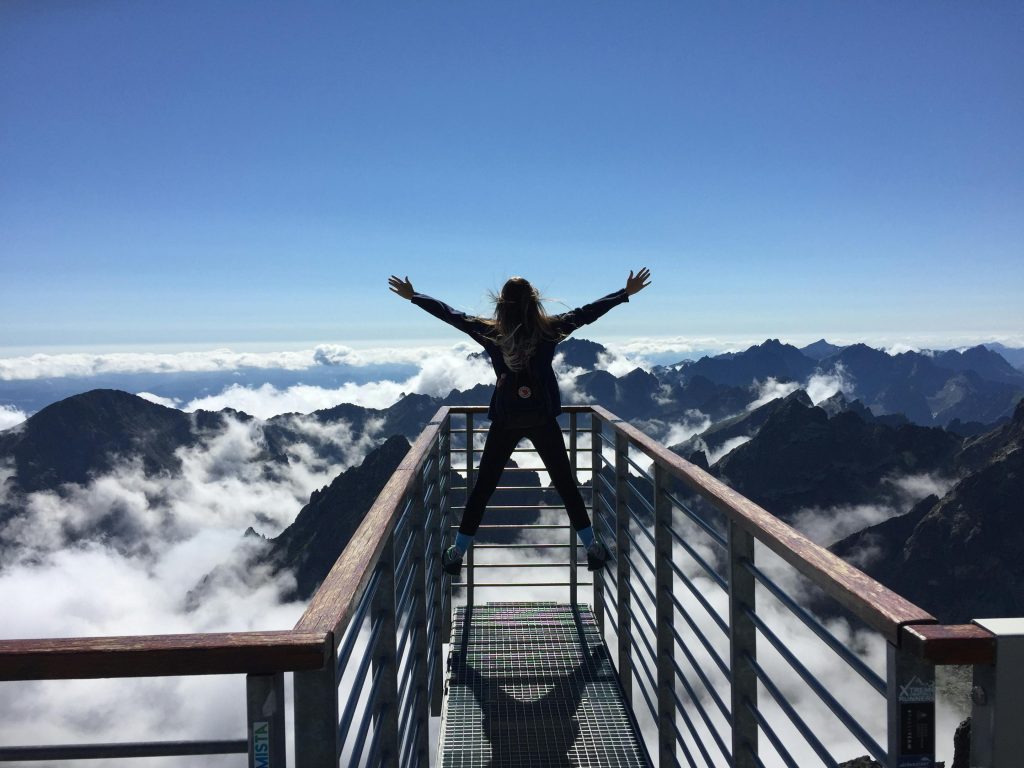 Person, die auf Handläufen mit weit geöffneten Armen Steht, Die Den Bergen und den Wolken gegenüberstehen